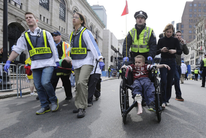 Офицер полиции Бостона везет в инвалидном кресле маленького мальчика, пострадавшего в результате взрыва.  (AP Photo/Charles Krupa)  