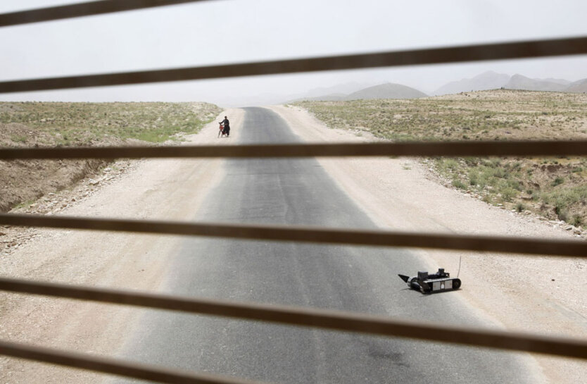 . Афганистан. Мальчик с велосипедом стоит на обочине дороги и наблюдает за роботом-сапером.