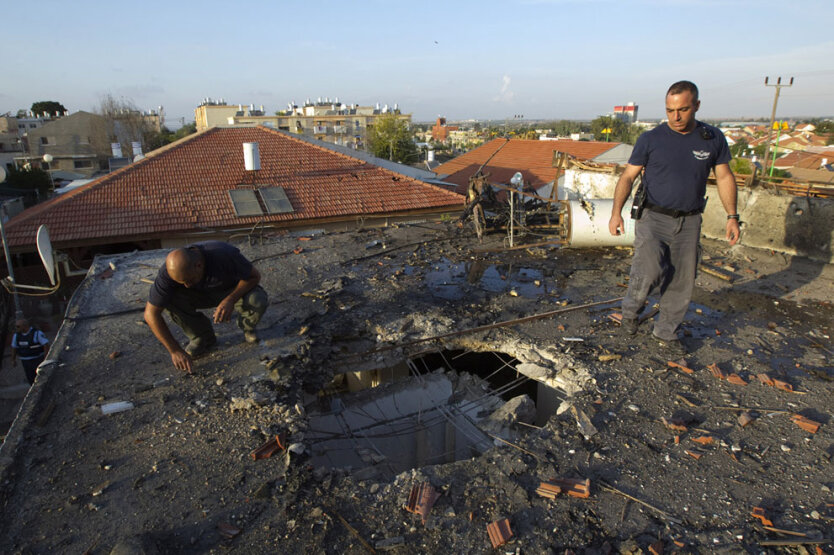 Специалисты по взрывчатым веществам из израильской полиции осматривают дыру после попадания палестинской ракеты  в южном городе Офаким