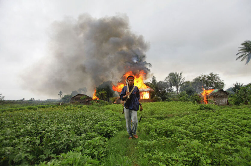 10 июня 2012. Этнический араканец идет с самодельным оружием в руках. На заднем плане горит здание, которое подожгли во время стычки между араканцами-буддистами и араканцами-мусульманами в Ситтве, Мьянма. 