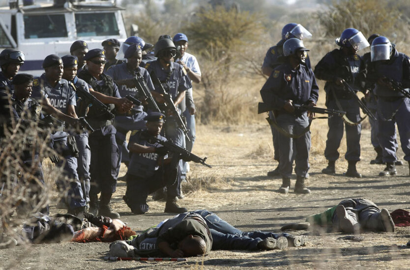 Полицейские смотрят на трупы застреленных ими бастующих шахтеров шахты в Рюстенбурге, что в 100 км к северо-западу от Йоханнесбурга.