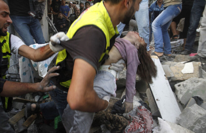 Работник аварийно-спасательных служб несет тело ребенка, найденного в доме после авиаудара израильских ВВС.