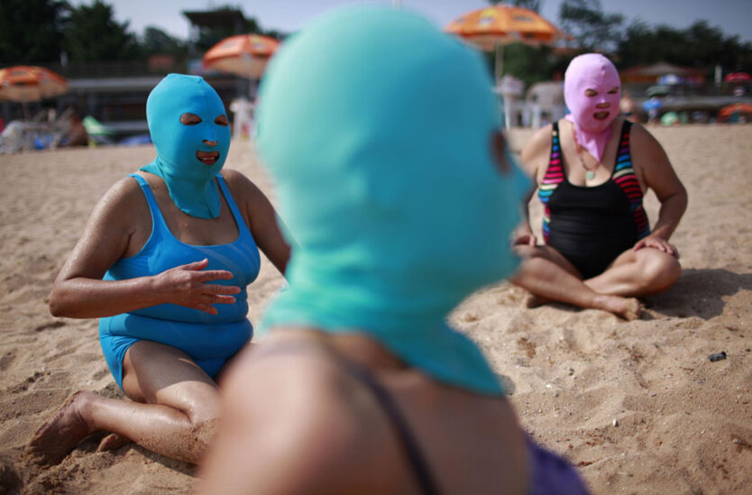 Женщины в специальных нейлоновых масках, защищающих лицо от ультрафиолета на  пляже в Циньдао, Китай