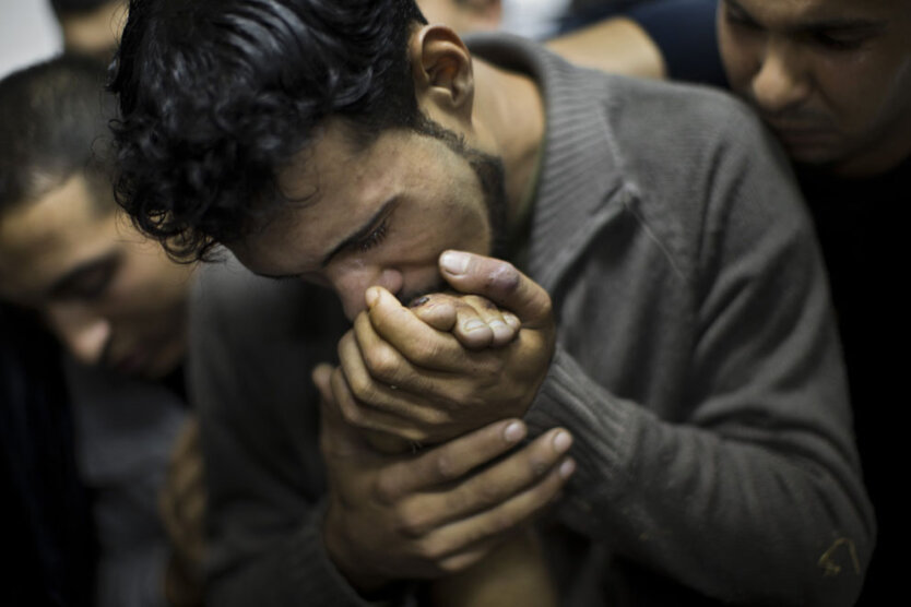 Палестинский мужчина целует руку мертвого родственника в морге больницы Шифа в городе Газа