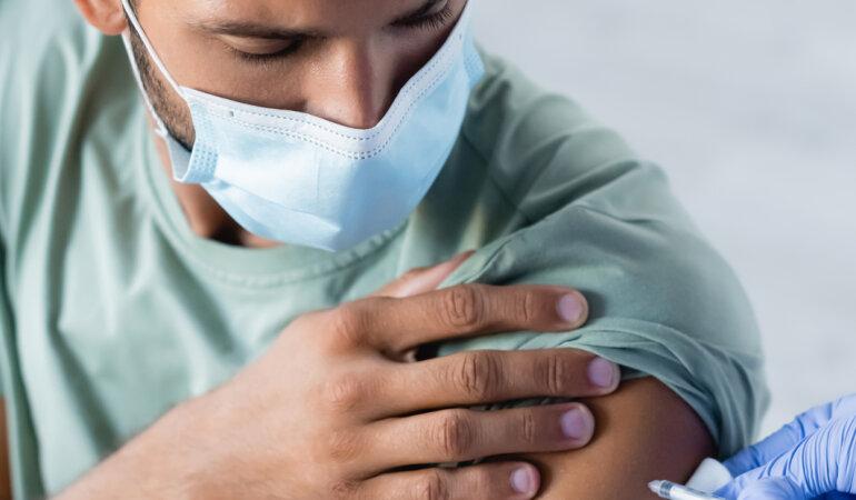 Вакцинация. Врач вакцинирует молодого человека в медицинской маске