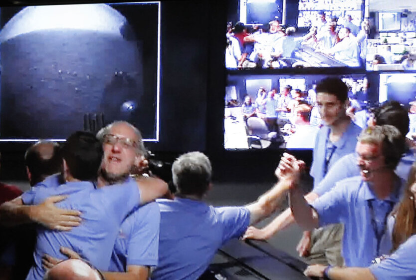 Стоп-кадр из видео, показывающего команду Mars Science Laboratory, которая радуется в Центре управления полетами НАСА первым кадрам, полученным от марсохода Curiosity (слева вверху), совершившего успешную посадку на Красную планету. 