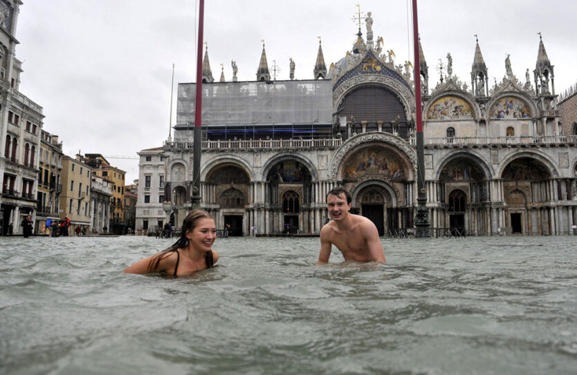 Мужчина и женщина плавают на затопленой площади Сан-Марко в Венеции, Италия