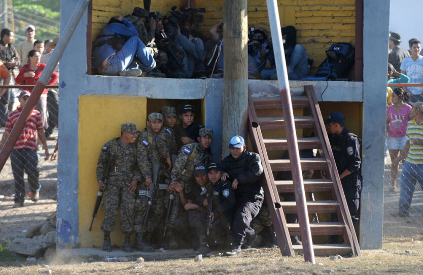 Полицейские с солдатами снизу и журналисты сверху прячутся во время вооруженного восстания заключенных  в Комайагуа, Гондурас, к северу от столицы Тегусигальпы, приведшего к гибели как минимум 360 человек. 