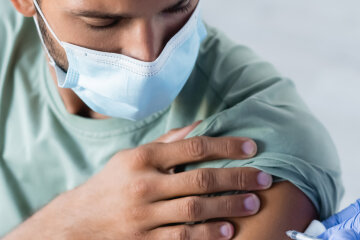 Вакцинация. Врач вакцинирует молодого человека в медицинской маске