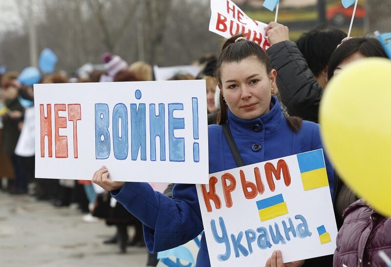 An anti-war protester holds placards during a rally on a road in Simferopol