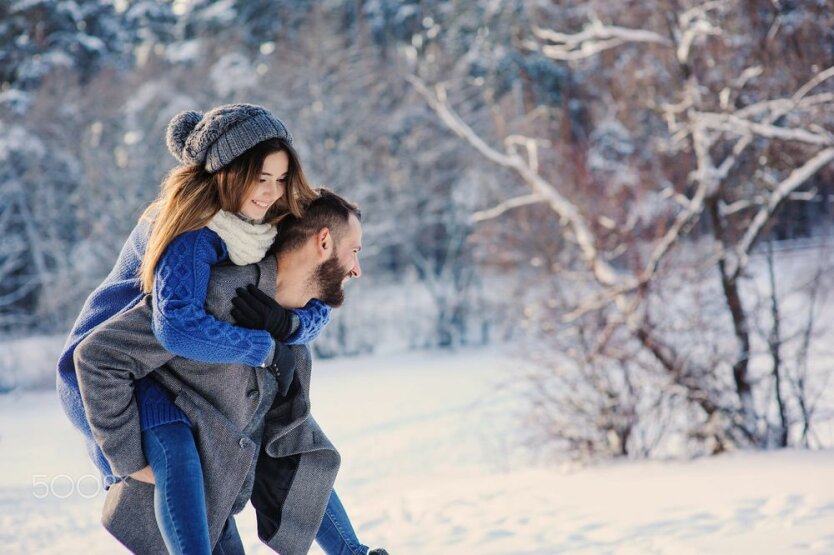 happy loving couple walking in snowy winter forest, spending christmas vacation together. Outdoor seasonal activities.
