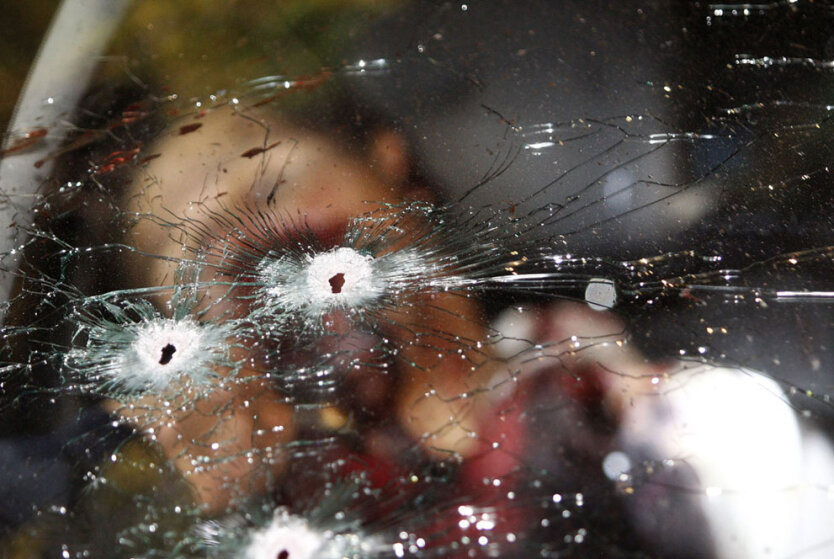 Труп бандита виднеется за изрешеченным пулями ветровым стеклом автомобиля в городе Хунгапео, штат Мичоакан, Мексика. 